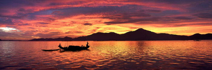 Fishing boat crosses the lagoon as a beautiful sunrise lights up the sky