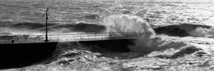panorama of Waves crashing against a pier in Porthleven Cornwall b&w