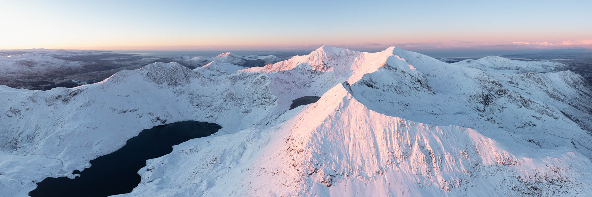 Aerial panorama of Crib Goch and Mount Snowdon covered in snow at sunrise