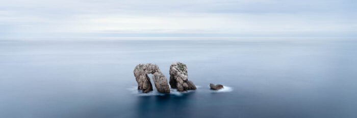 Panorama of serene blue water surround the Urro del Manzano Arch in Spain