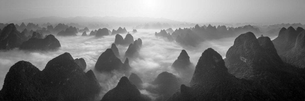 Black and white aerial panorama of the Xingping Karst mountain peaks above the clouds in Yangshuo, China